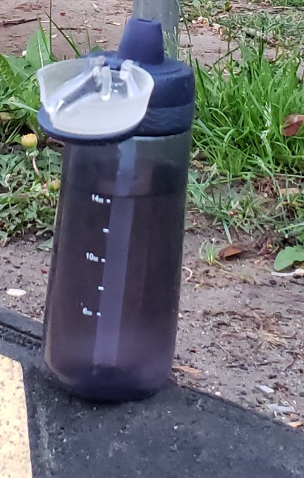 Gray water flask set on a black curb by a neighborly finder
